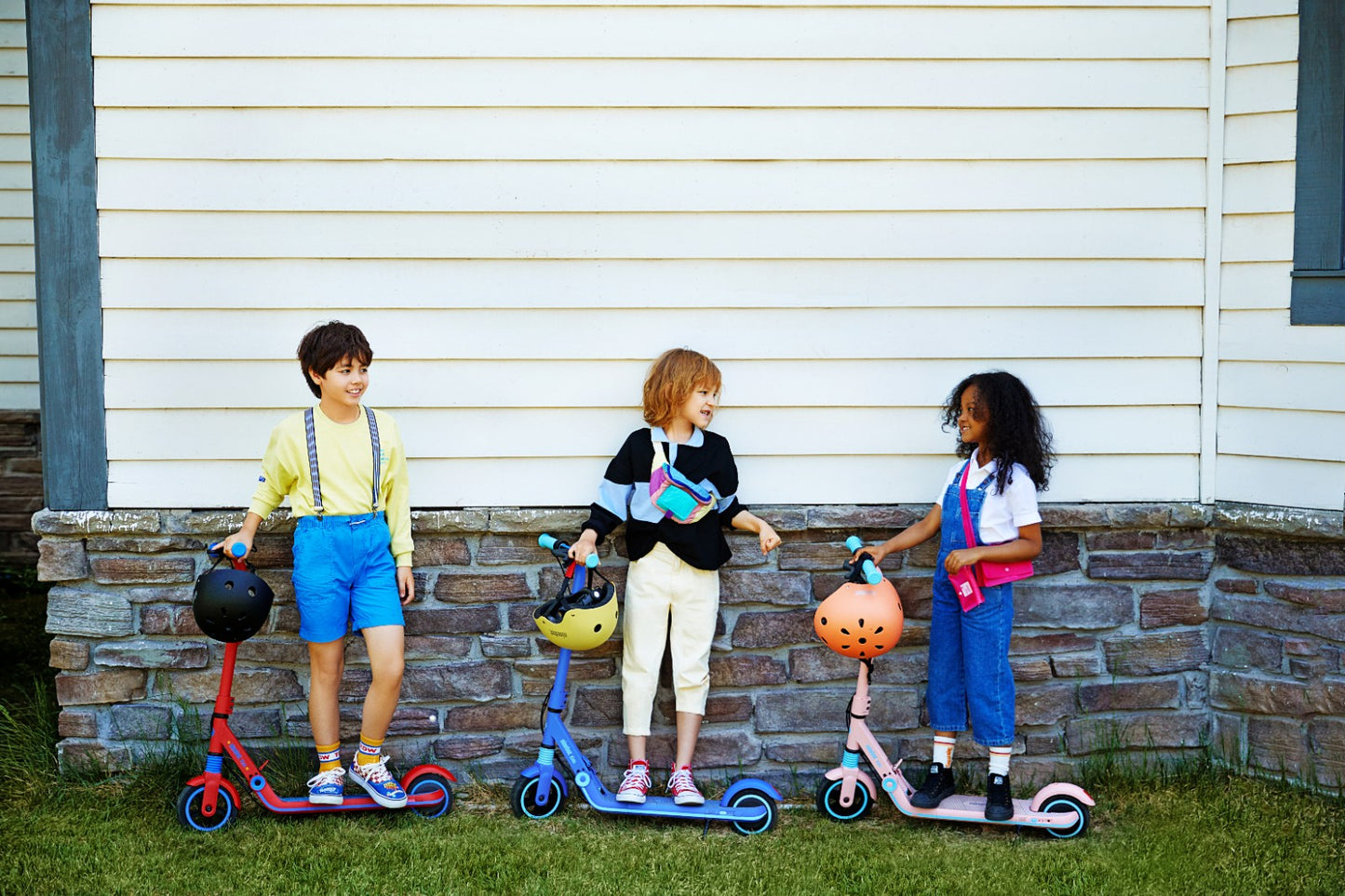 Three kids standing next to a wall each with a Segway Ninebot zing e8 electric kickscooter for kids. One Blue, one pink, one red.