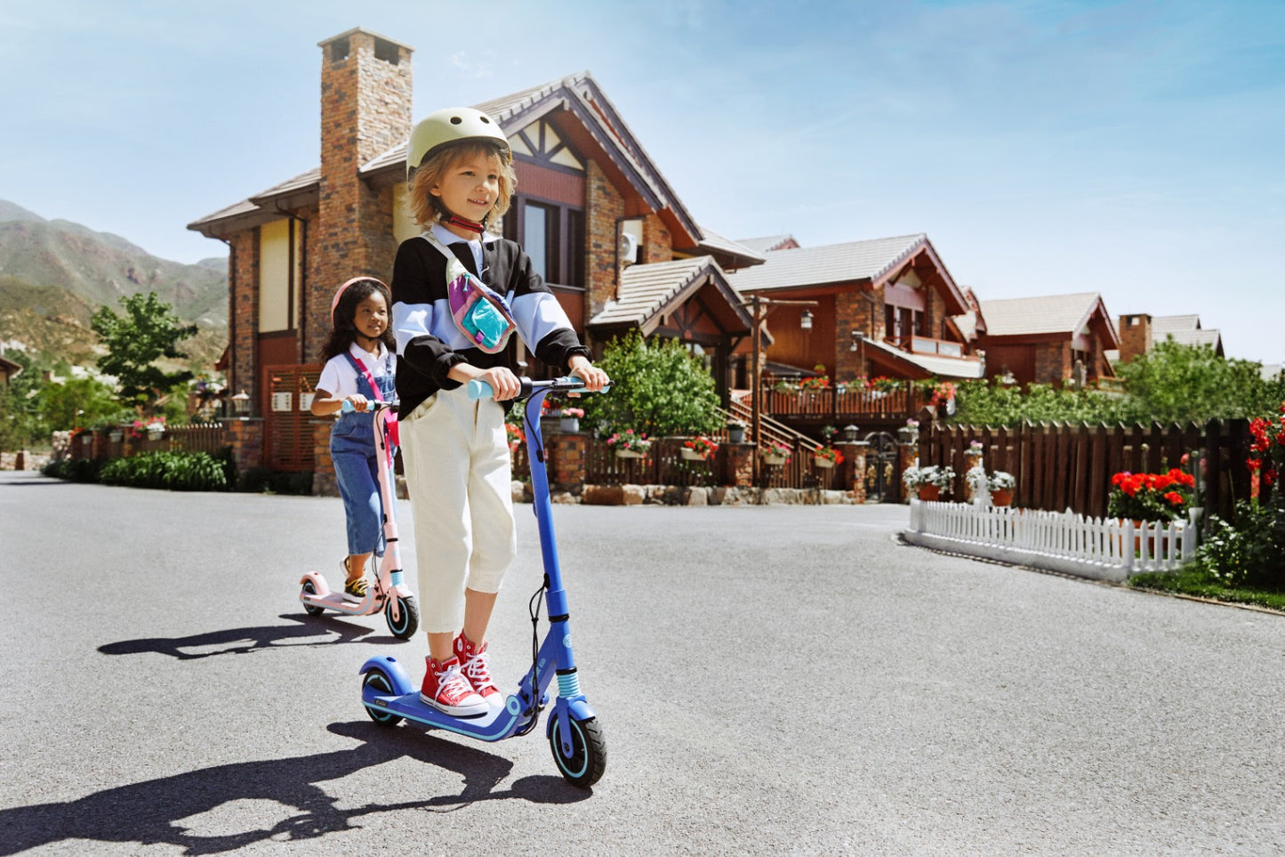 Two kids riding the Ninebot Zing e8 electric kickscooter on the street wearing helmets.