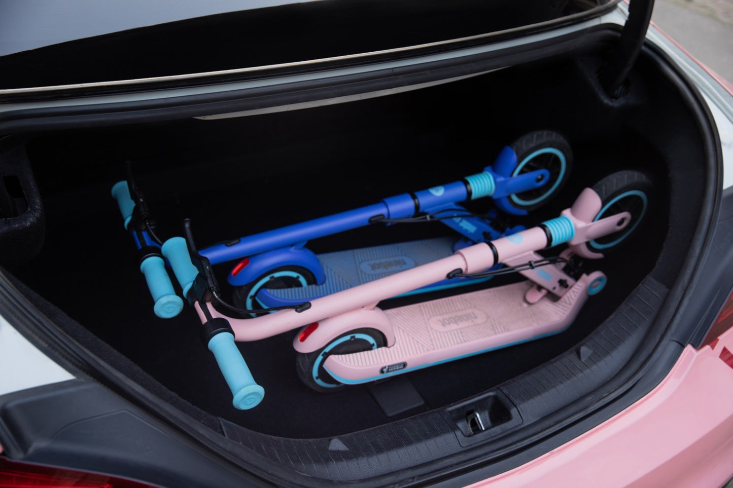 Two ninebot zing e8 in the trunk of a car. Folded and portable. One blue and one pink.